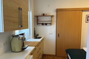 Eine kleine Küche mit Kaffeemaschine, Holzschränken, einem Waschbecken und einem kleinen Regal mit Tassen.