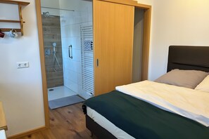 Un dormitorio con cama, un armario de madera, zona de ducha con puerta de vidrio y estante con tazas.