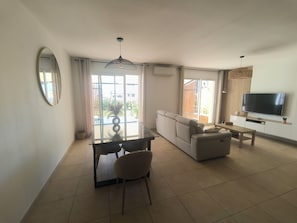 Un salon moderne avec un canapé, une table à manger et des chaises, un téléviseur et une grande fenêtre.