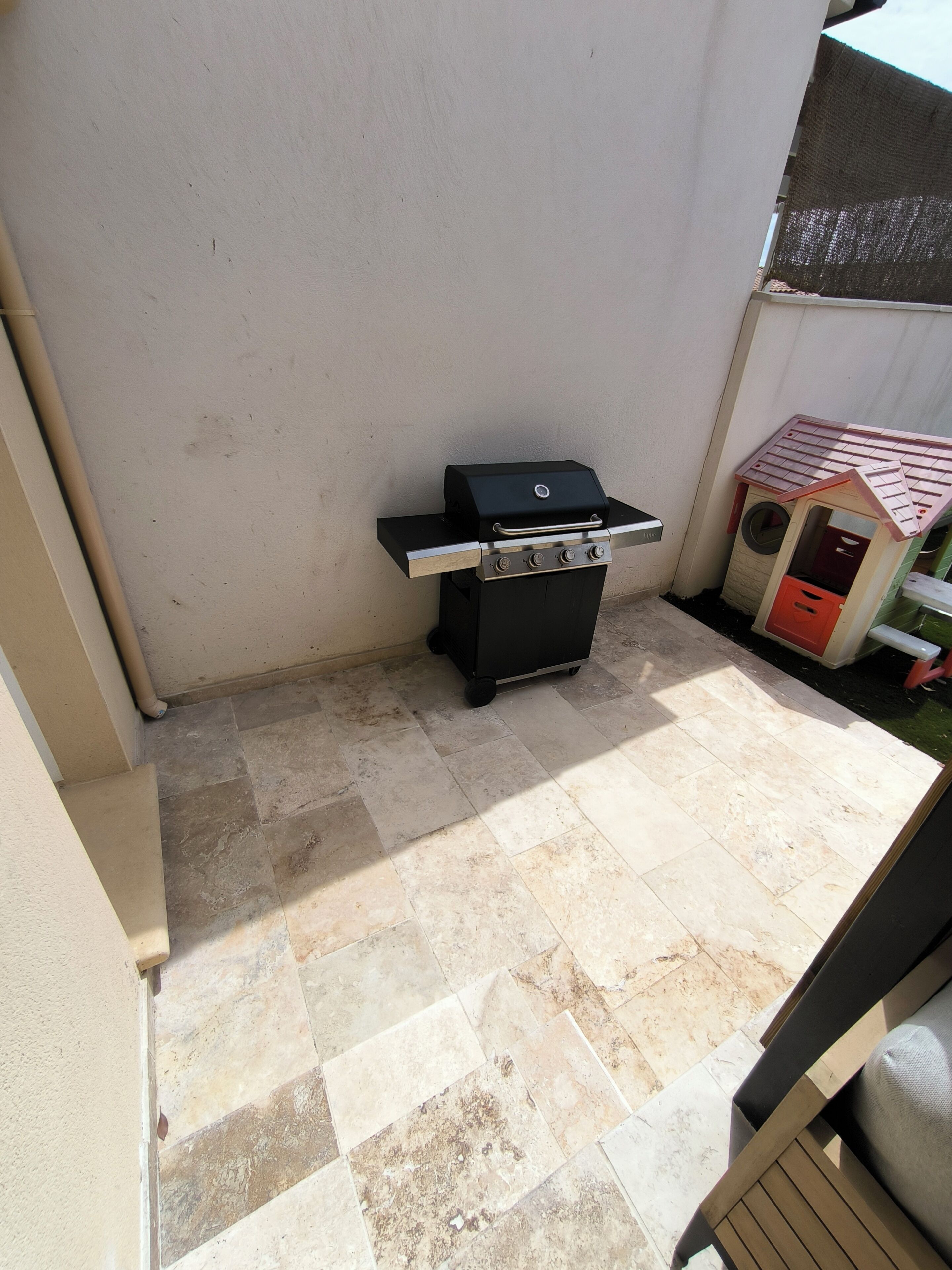 A patio area with a grill, a small playhouse, and tiled flooring.