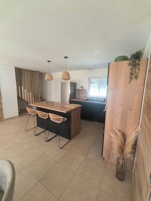 Una cocina moderna con una isla de madera, dos lámparas colgantes y vistas al salón.