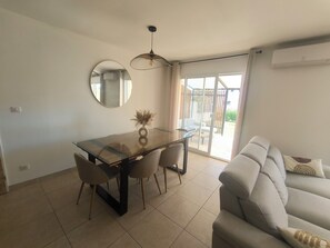 A dining area with a glass table, chairs, a round mirror, and a hanging light fixture. - 3-bedroom villa with garage, covered terrace and air-conditioned pétanque court (Raphele les Arles)