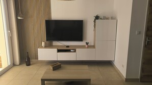A modern living room with a flat-screen TV, wooden flooring, a coffee table, and a pendant light.