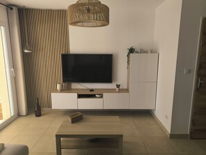 A modern living room with a flat-screen TV, wooden flooring, a coffee table, and a pendant light. - 3-bedroom villa with garage, covered terrace and air-conditioned pétanque court (Raphele les Arles)