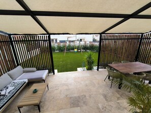 Une terrasse couverte avec un canapé, une table et des chaises, une pelouse et une clôture en bois.