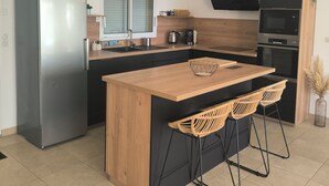 A modern kitchen with a stainless steel refrigerator, wooden island, black cabinets, and wicker chairs.
