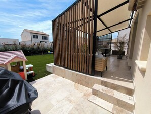 En overdækket terrasse med træhegn, udendørs møbler og et lille legehus.