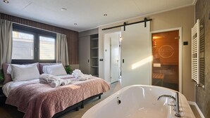 Une chambre moderne avec un grand lit, une baignoire et une porte coulissante donnant accès à un espace douche.