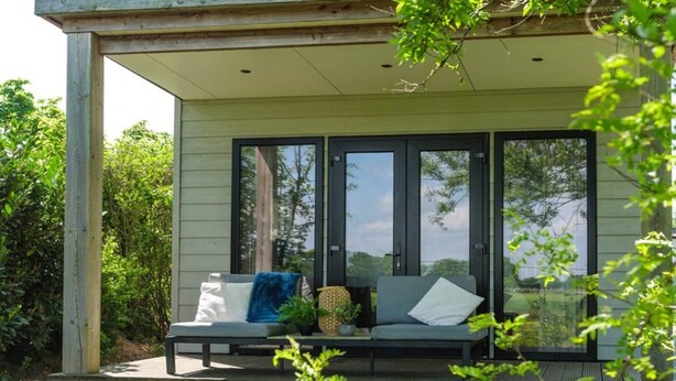 Un espace extérieur abrité, aménagé avec un banc et des coussins, et entouré de verdure.