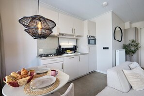 Una cocina moderna con gabinetes blancos, una lámpara colgante negra y un comedor con una mesa dispuesta para dos personas.