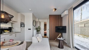 Une chambre d’hôtel moderne équipée d’une kitchenette, d’un canapé, d’une télévision et d’une grande fenêtre.