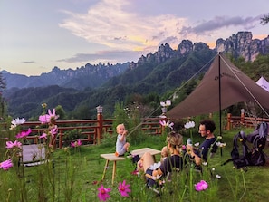 A group of people sitting on a grassy hill with a tent and a wooden table, overlooking a mountainous landscape. - Tangwan Mountain Homestay - Yangjiajie  (Zhangjiajie)