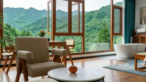 A room with a large window, a bathtub, a round table, and a sofa. - Shiyi Tangwan Yangjiajie Lodge (Zhangjiajie)