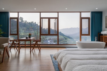A bedroom with a large window, a bathtub, a bed, and a table with chairs.. Tangwan Mountain Homestay - Yangjiajie
