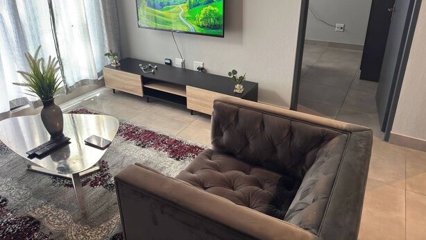 Una sala de estar moderna con un sofá, una mesa de centro, un televisor en la pared y una planta.