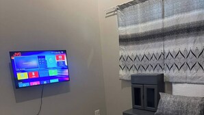 Un dormitorio con cama, televisor montado en la pared, mesita de noche y ventana con cortinas estampadas.