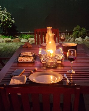 A dining table set outdoors with a candle, wine glass, and plates.