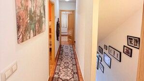 A hallway with a patterned carpet, a large abstract painting on the left wall, and several framed pictures on the right wall.
