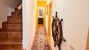 A hallway with a patterned carpet, a wooden staircase, and a ship's wheel decoration on the wall.