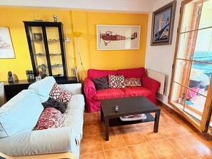 A living room with a red sofa, a blue sofa, a dark coffee table, a glass cabinet, and a large window with a view.