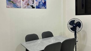 Een eetgedeelte met een tafel, stoelen, een ventilator en drie bloemen schilderijen aan de muur.