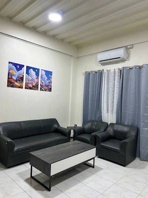 A living room with a black leather sofa, a coffee table, and a wall-mounted air conditioner. - Jaz Urban Stay - 337F (Angeles)
