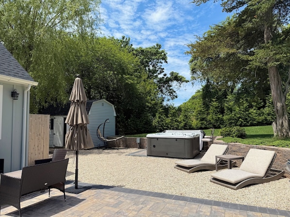 A patio area with a hot tub, lounge chairs, and a pergola with an umbrella. - Peaceful and Private 4-Bedroom Home in Southampton (Southampton)