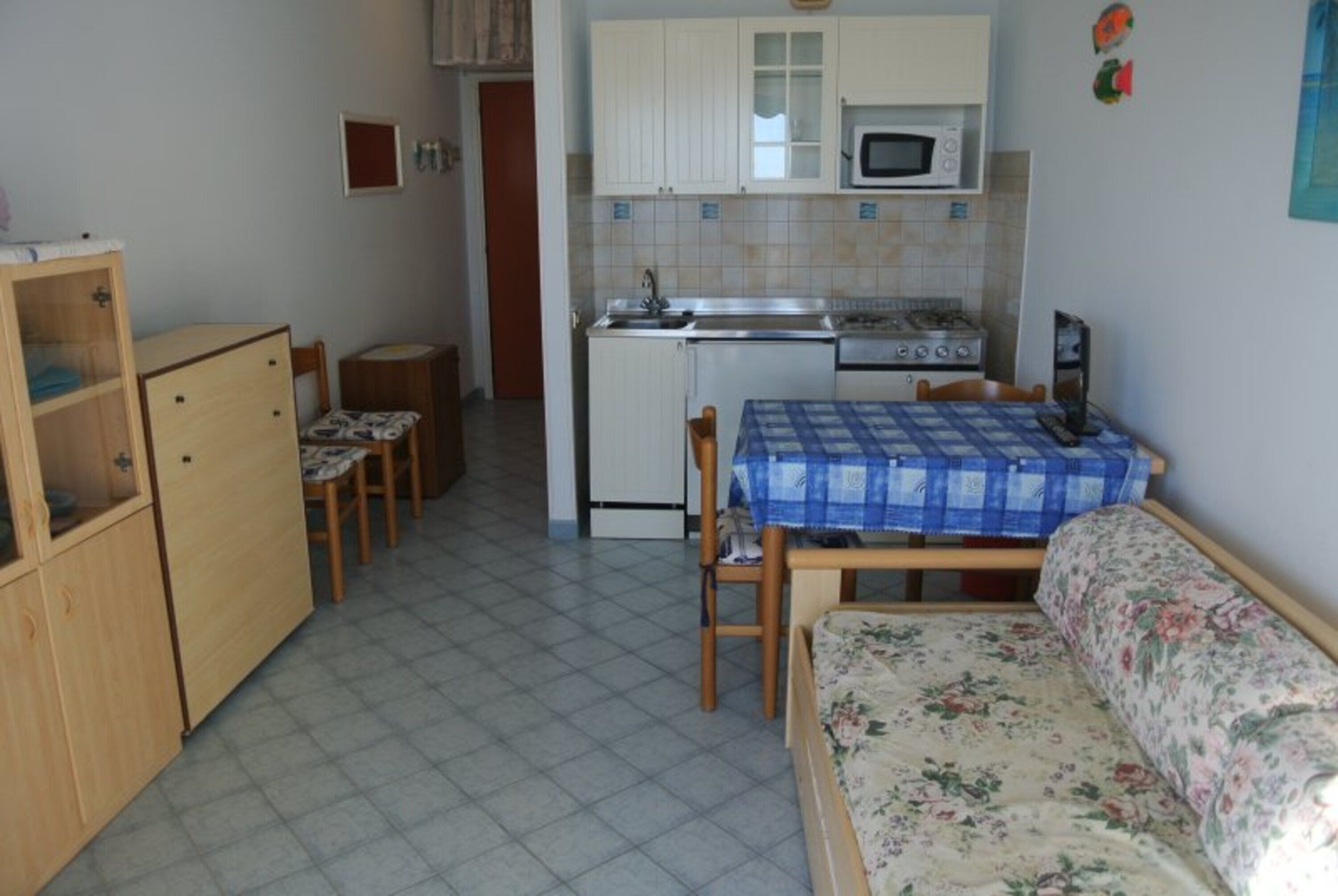 A compact kitchen with a microwave, stove, and sink. There is a dining table with a blue tablecloth and a floral sofa.