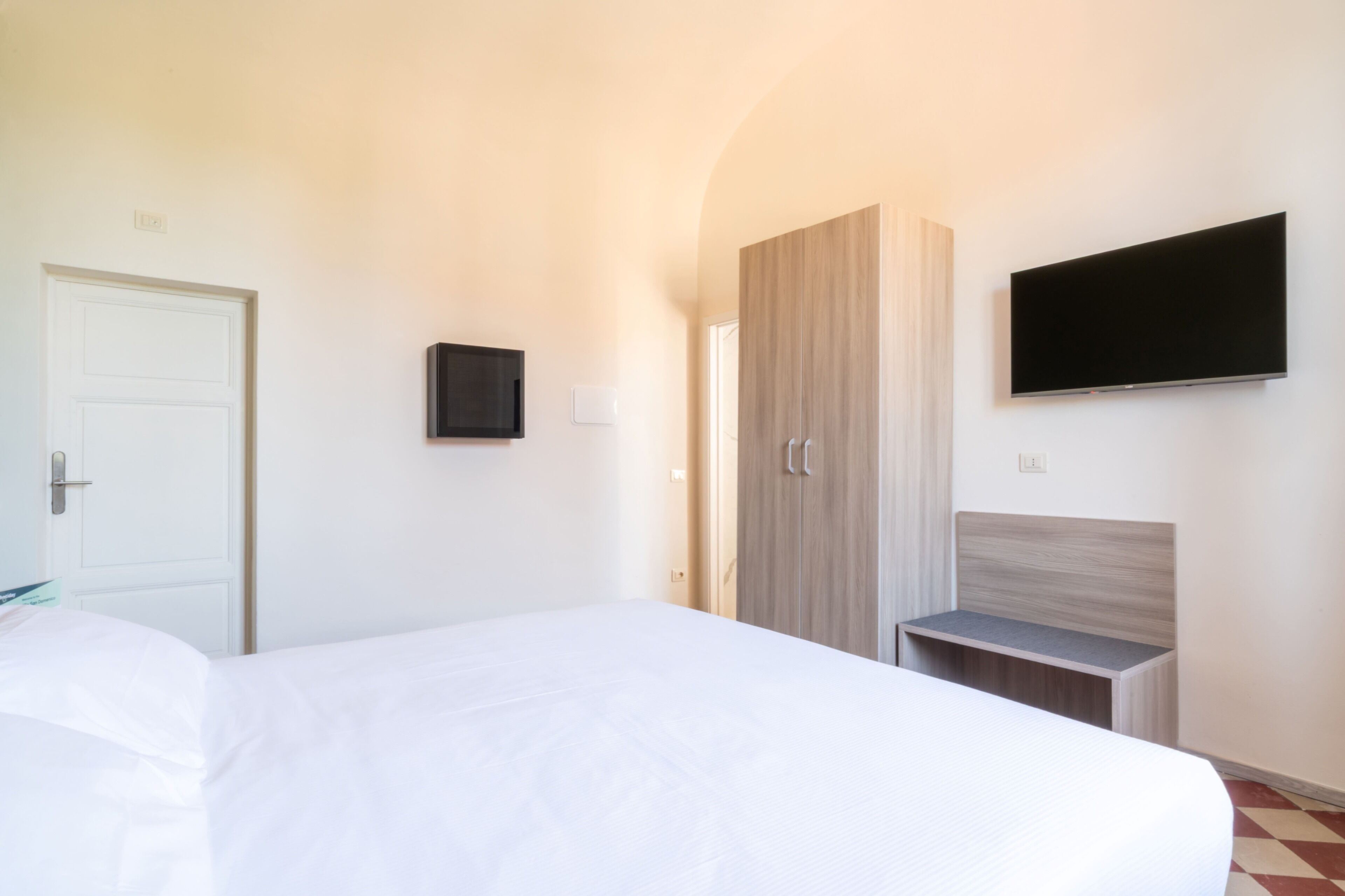Een hotelkamer met een bed, een kledingkast, een televisie en een tafeltje.