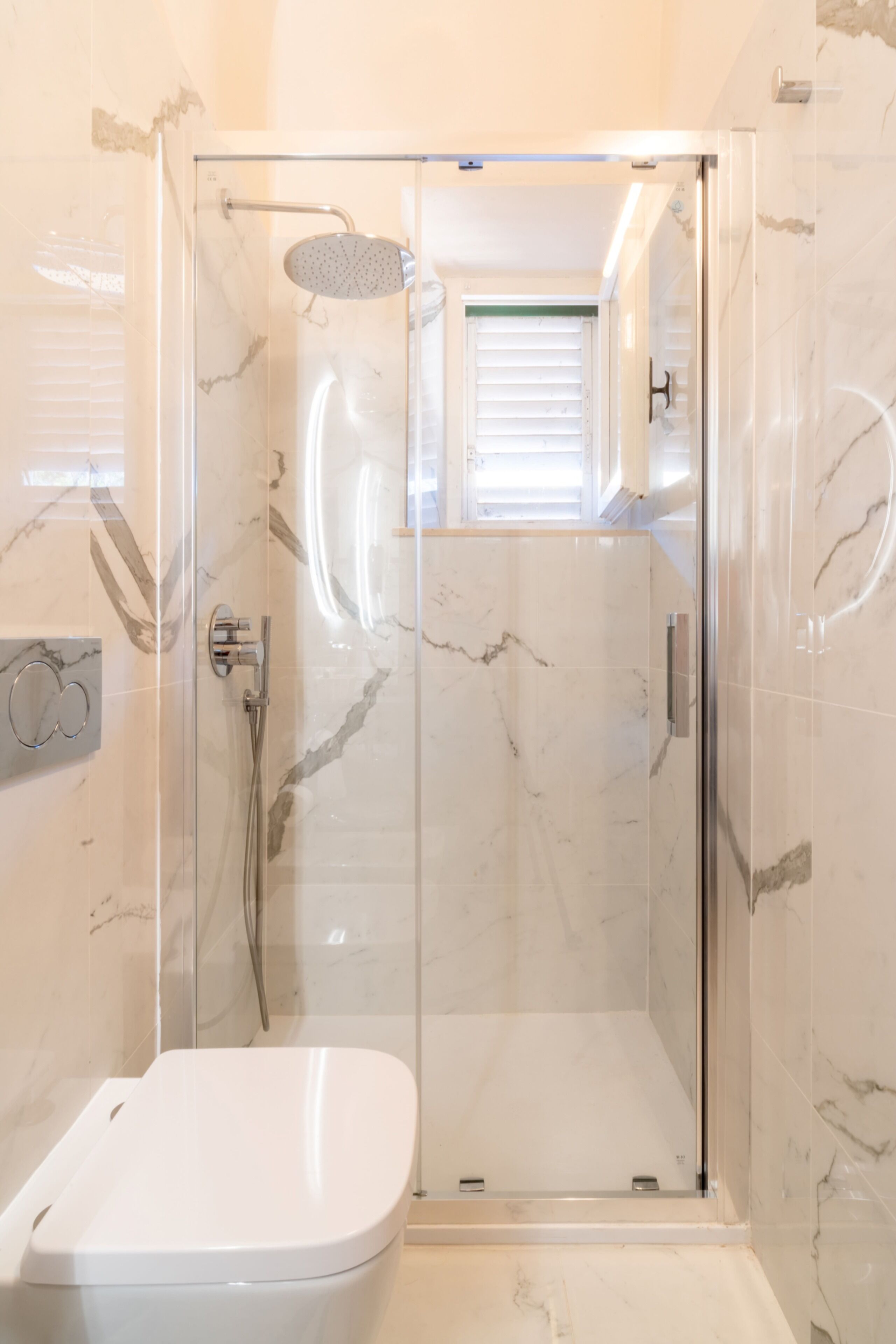 Eine Duschkabine mit Handbrause, ein am Wand montierter Wasserhahn und eine Toilette.