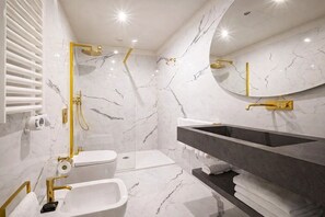 Un baño moderno con inodoro blanco, un bidé, un lavabo con un mueble grande y una ducha con detalles dorados.