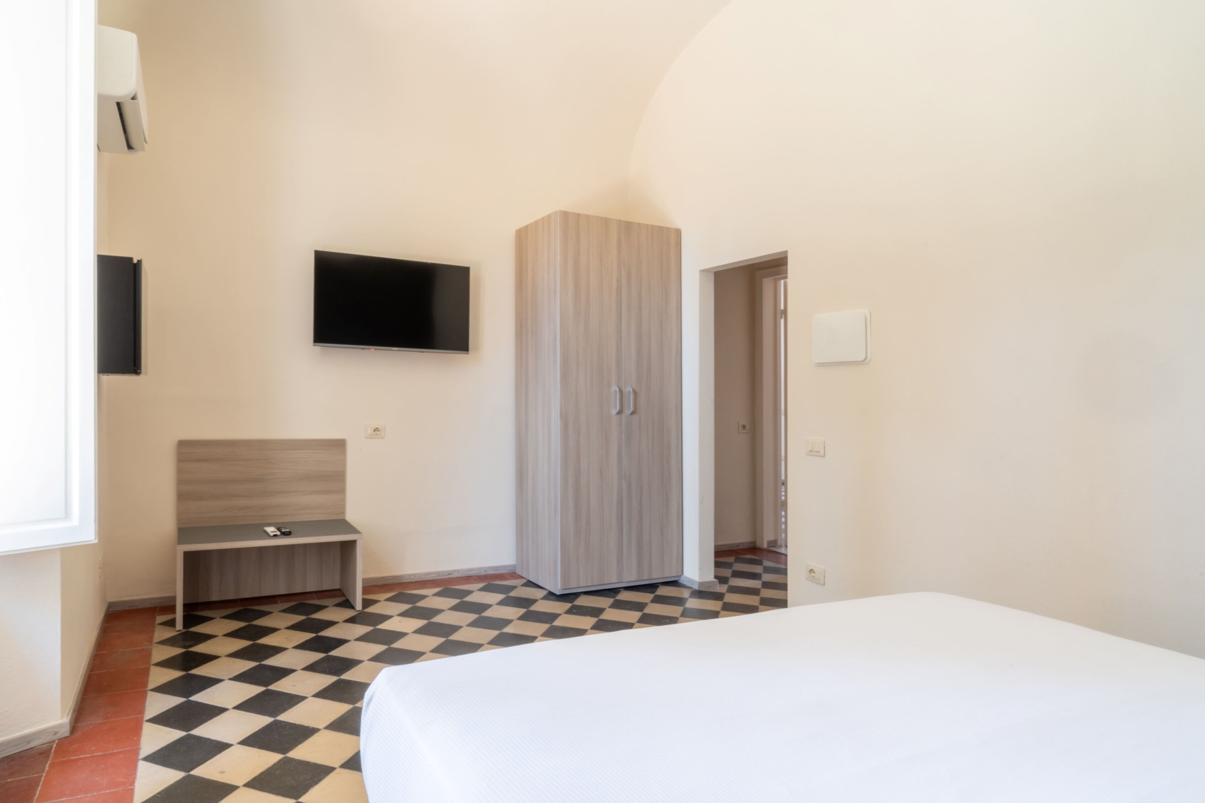 Ein Schlafzimmer mit einem Bett, einem Fernseher, einem Kleiderschrank und einer Sitzbank.