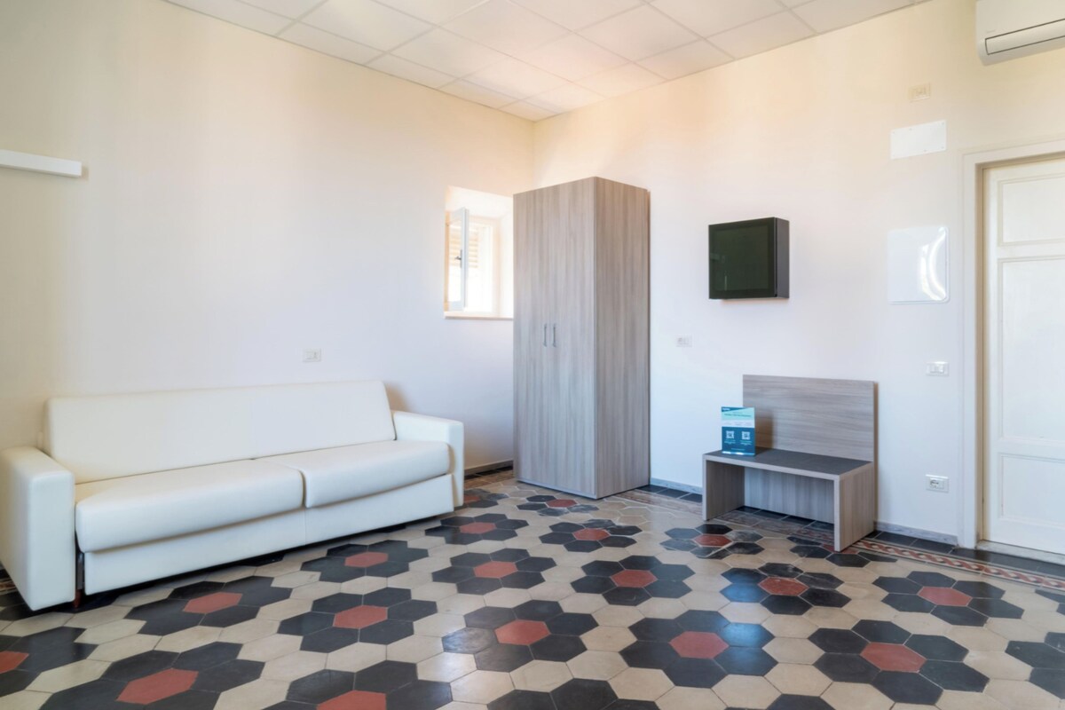 Una habitación con un sofá blanco, un armario, una mesita y un televisor montado en la pared.