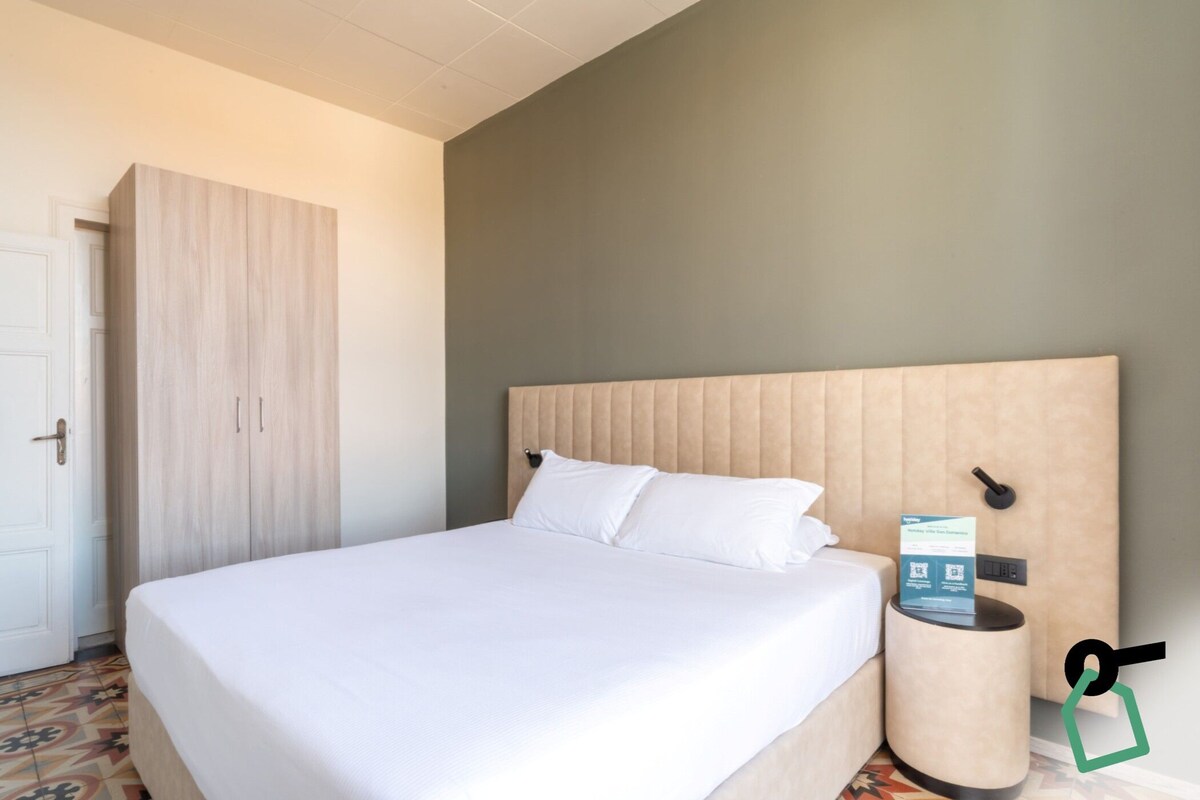 Una habitación de hotel con una cama, una mesita de noche, un teléfono en la pared y una puerta.