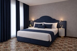 Una habitación de hotel con una cama grande, dos mesitas de noche, un cabecero y baldosas de suelo estampadas.