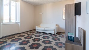 A room with a white sofa, a patterned floor, a flat-screen TV, and a wooden panel on the wall. - Hotiday Villa San Domenico (Rosignano Marittimo)