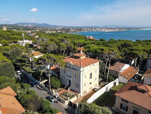 Un pueblo costero con un edificio destacado que tiene techo de tejas rojas y fachada blanca, rodeado de abundante vegetación y una vista despejada del mar.