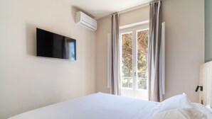 A hotel room with a bed, a flat-screen TV mounted on the wall, and a window with curtains. - Hotiday Villa San Domenico (Rosignano Marittimo)