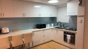 A modern kitchen with white cabinets, a black microwave, a kettle, and a sink with a faucet. - Modern 2BR Apartment with Free Parking | Near Perth CBD & Beaches. (Wembley)