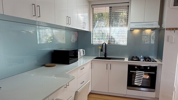 A modern kitchen with white cabinets, a black stove, and a window with blinds.