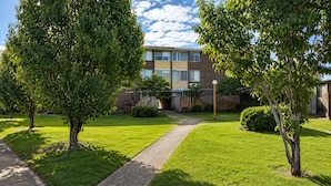 A residential building with a paved pathway, green lawn, and trees.
