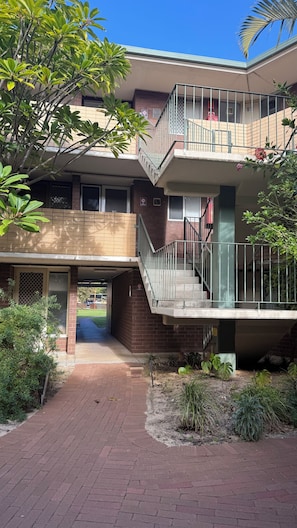 A multi-story building with a central staircase, a covered entrance, and surrounding greenery. - Modern 2BR Apartment with Free Parking | Near Perth CBD & Beaches. (Wembley)