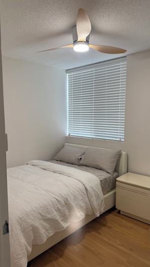 A bedroom with a bed, a nightstand, a ceiling fan, and a window with blinds. - Modern 2BR Apartment with Free Parking | Near Perth CBD & Beaches. (Wembley)