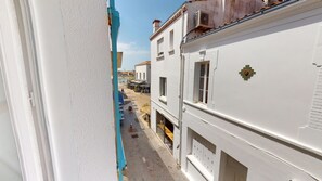 A narrow street with white buildings, a blue door, and a small shop with outdoor seating. - HAUBAN - Charm & Authenticity in the Old Port (Saint-Gilles-Croix-de-Vie)