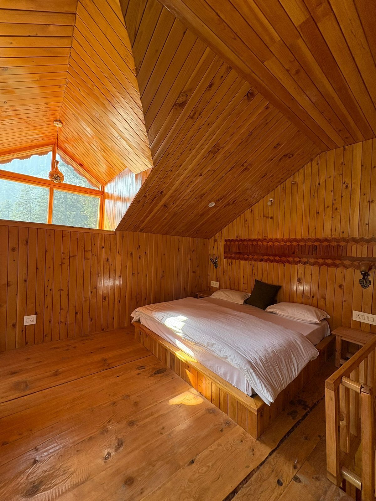 A wooden cabin bedroom with a bed, a window, and a wooden staircase.