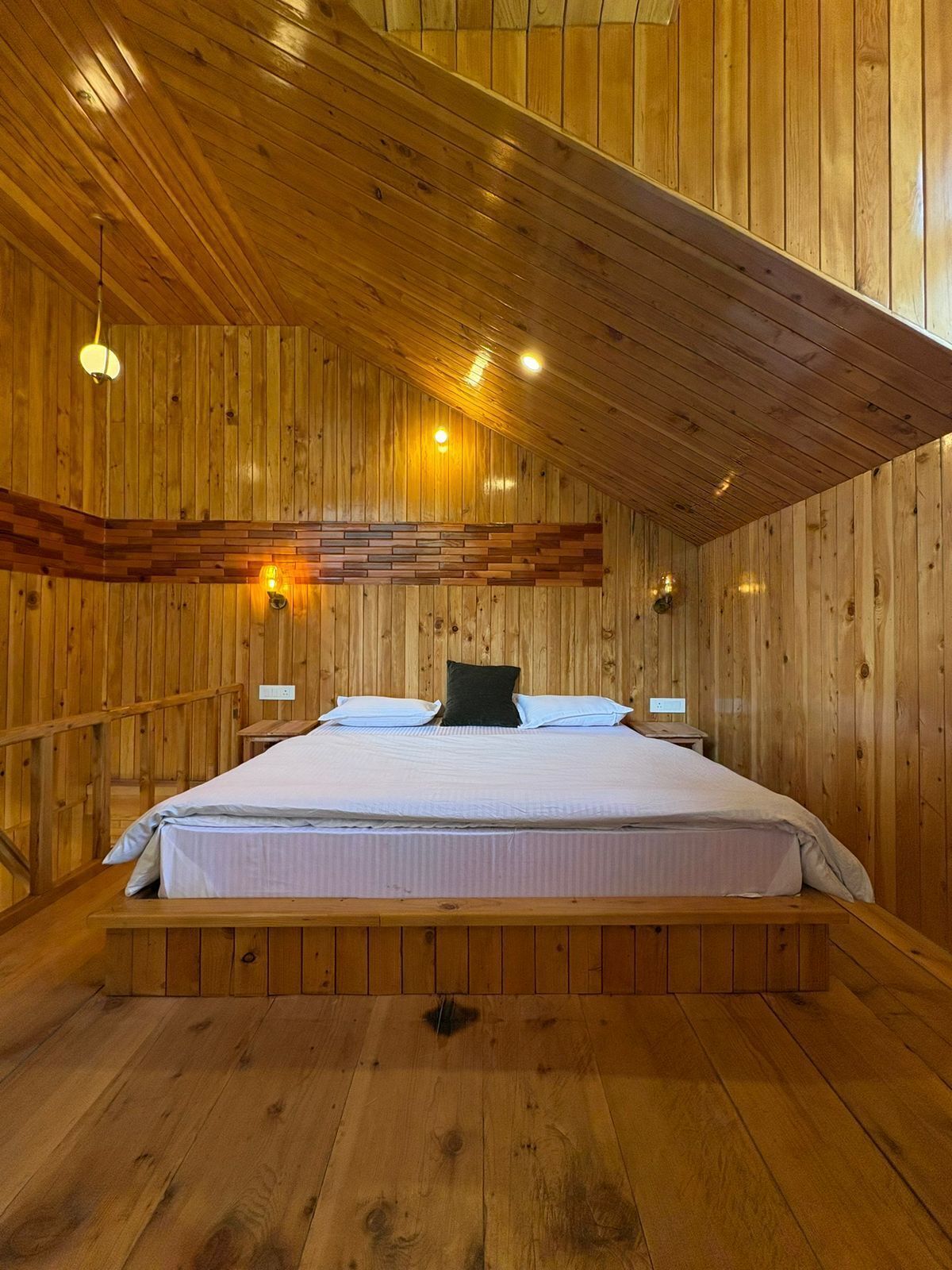 Una habitación con paneles de madera, una cama, dos mesitas de noche y techo inclinado.