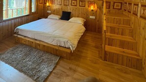 Interior de una cabaña de madera con una cama, escaleras y cuadros en las paredes.