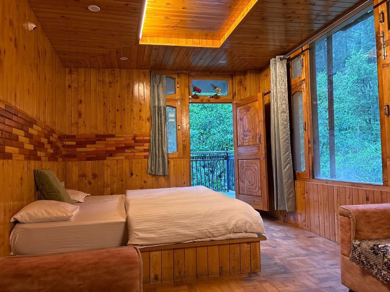 Une chambre dans une cabane en bois, avec un lit, deux chaises et un balcon donnant sur la forêt.