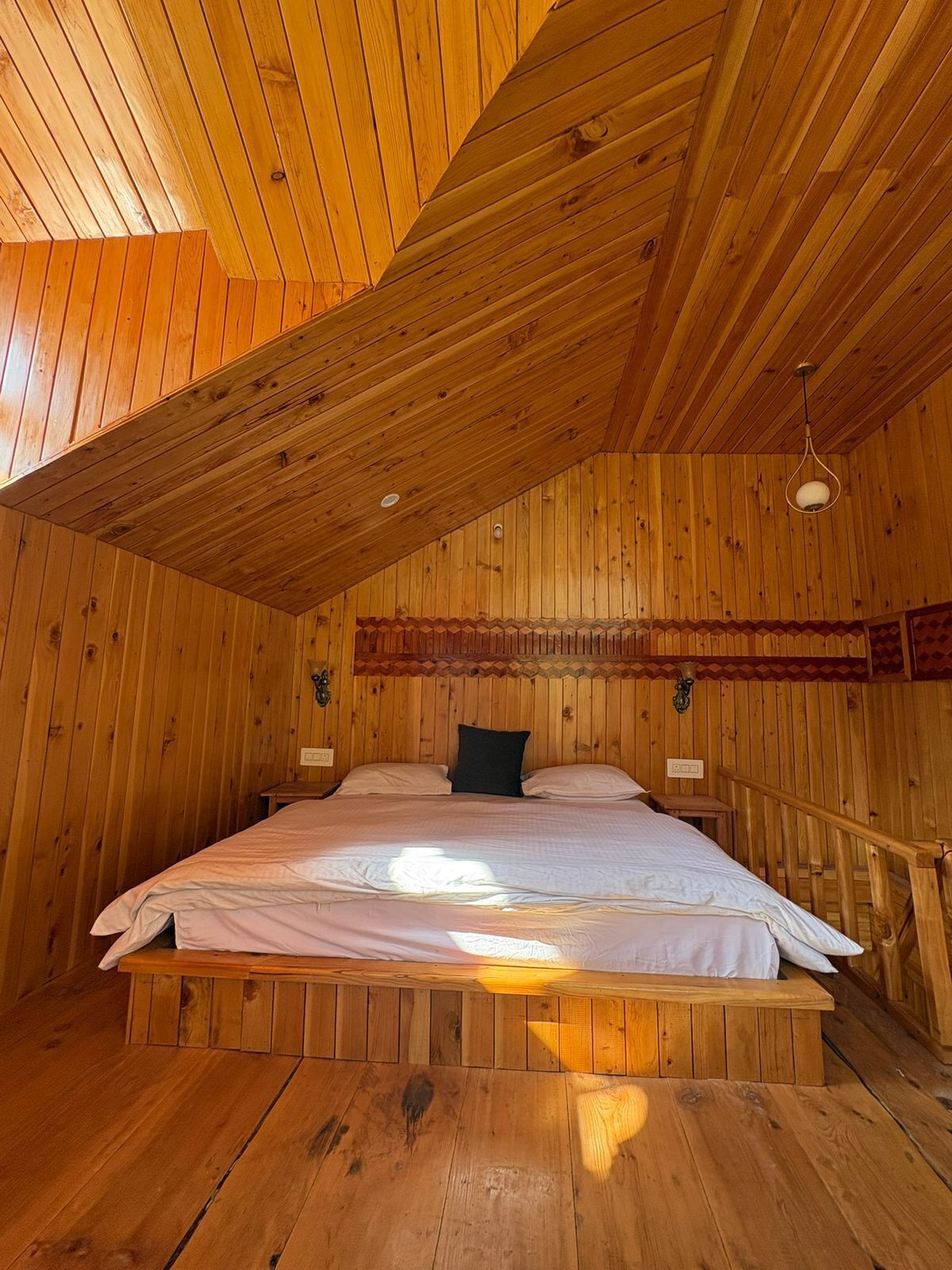 A wooden cabin bedroom with a sloped ceiling, a bed with white bedding, and a small bedside table.