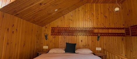A wooden cabin bedroom with a sloped ceiling, a bed with white bedding, and a small bedside table.